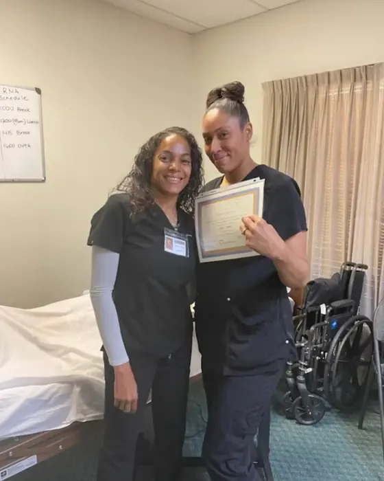 A smiling graduate showing her nursing assistant certificate in the skills lab