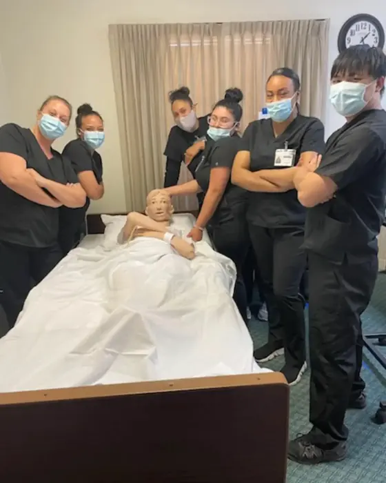 A class posing with the training manikin after a hands-on practice session